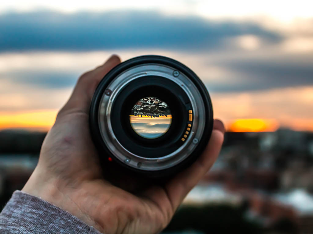 A person holding a camera lens up to a sunset
