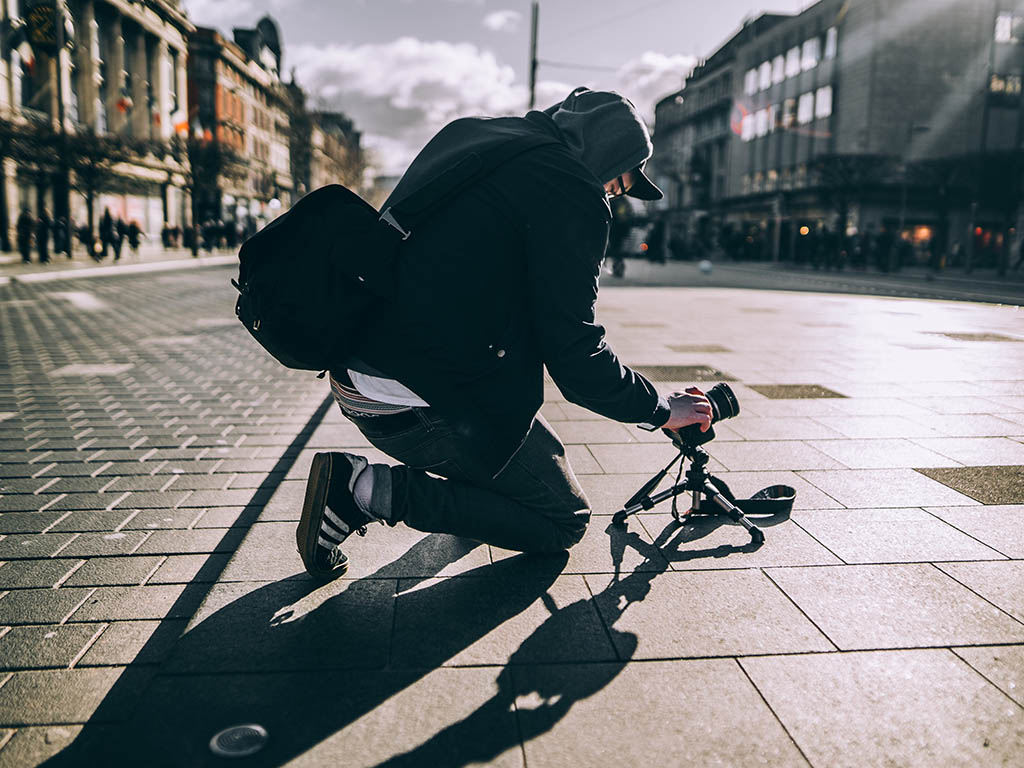 Photo of a man kneeling on the ground adjusting a camera on a tripod