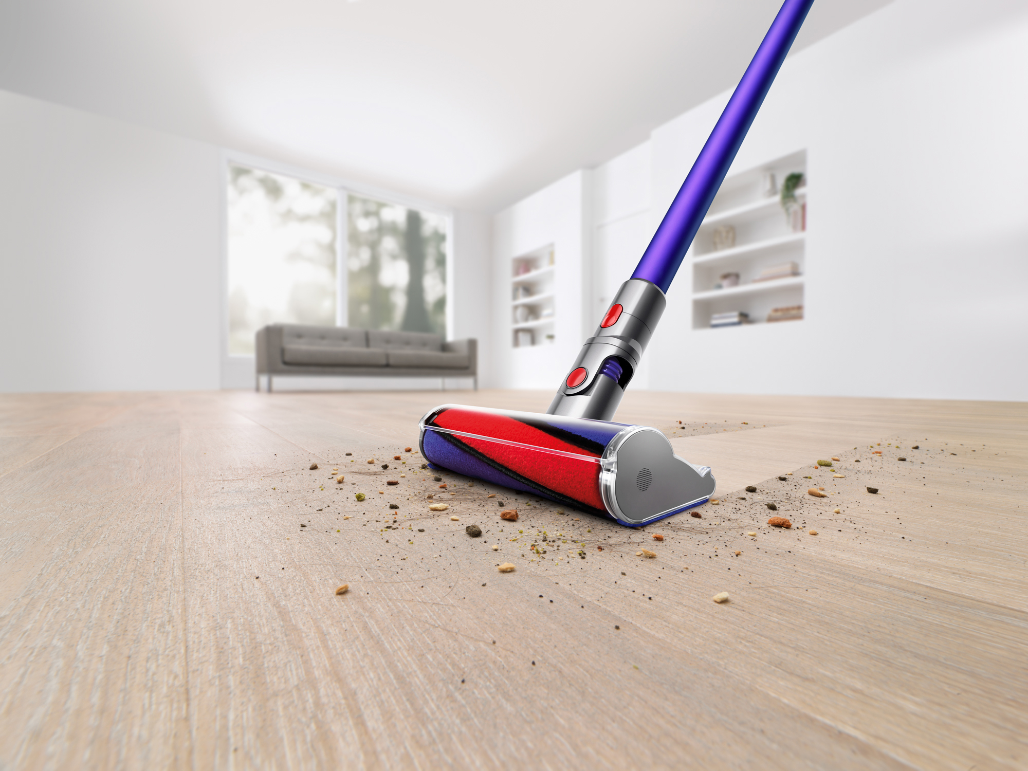 The Dyson V11 Absolute Pro Cordless Stick Vacuum is shown cleaning a hardwood floor in a white room. It makes a clean sweep through the dust and debris on the floor, leaving nothing behind it.