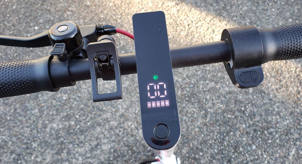 This image shows the scooter's handlebars with bell, hand brake, speedometer, battery level indicator, and accelerator