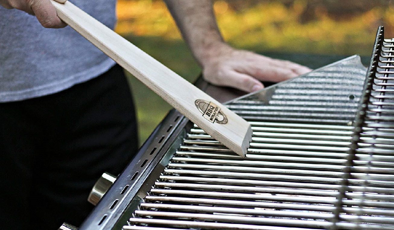 image of a person using a wooden BBQ scraper to clean a BBQ grate