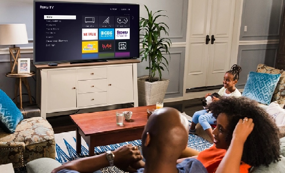 image of a family watching a Roku Smart TV displaying the Roku menu