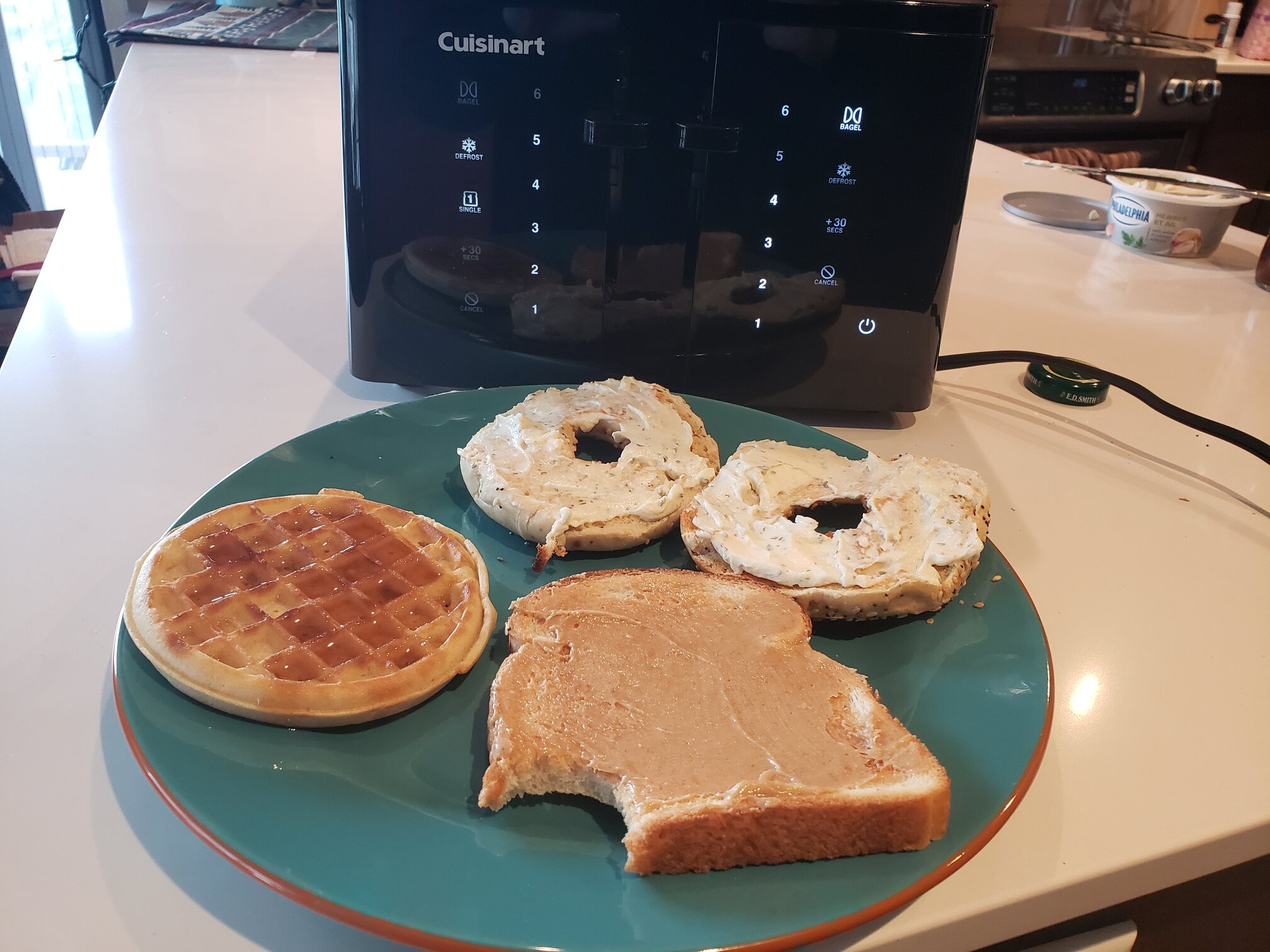 image of the toaster next to toasted bagels, bread, and a waffle