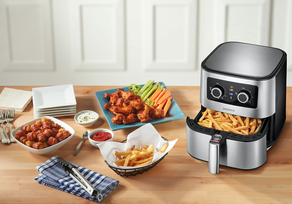 An Insignia air fryer with various dishes beside it.