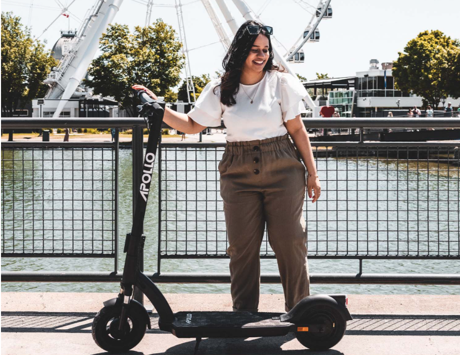A woman standing beside an electric scooter as her mode of etransportation.