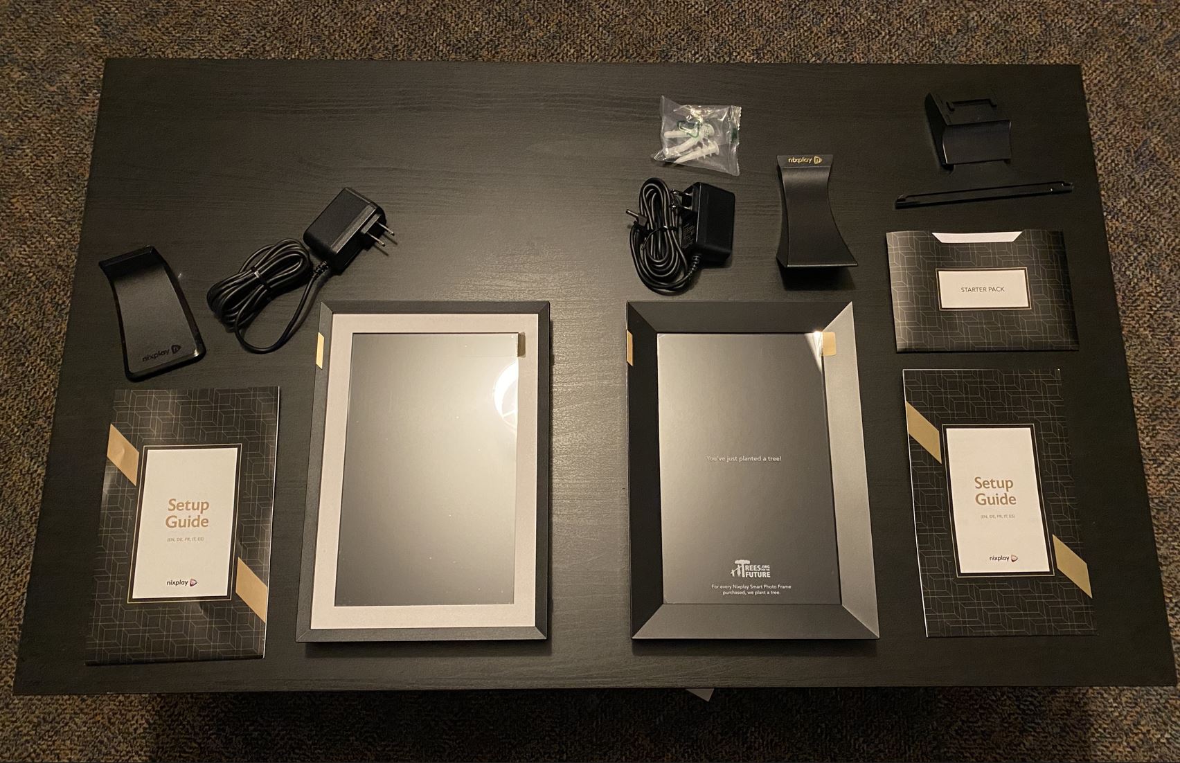 Instruction manual and parts of both Classic white and New Black Touch 10 Smart Frames by Nixplay on a black coffee table