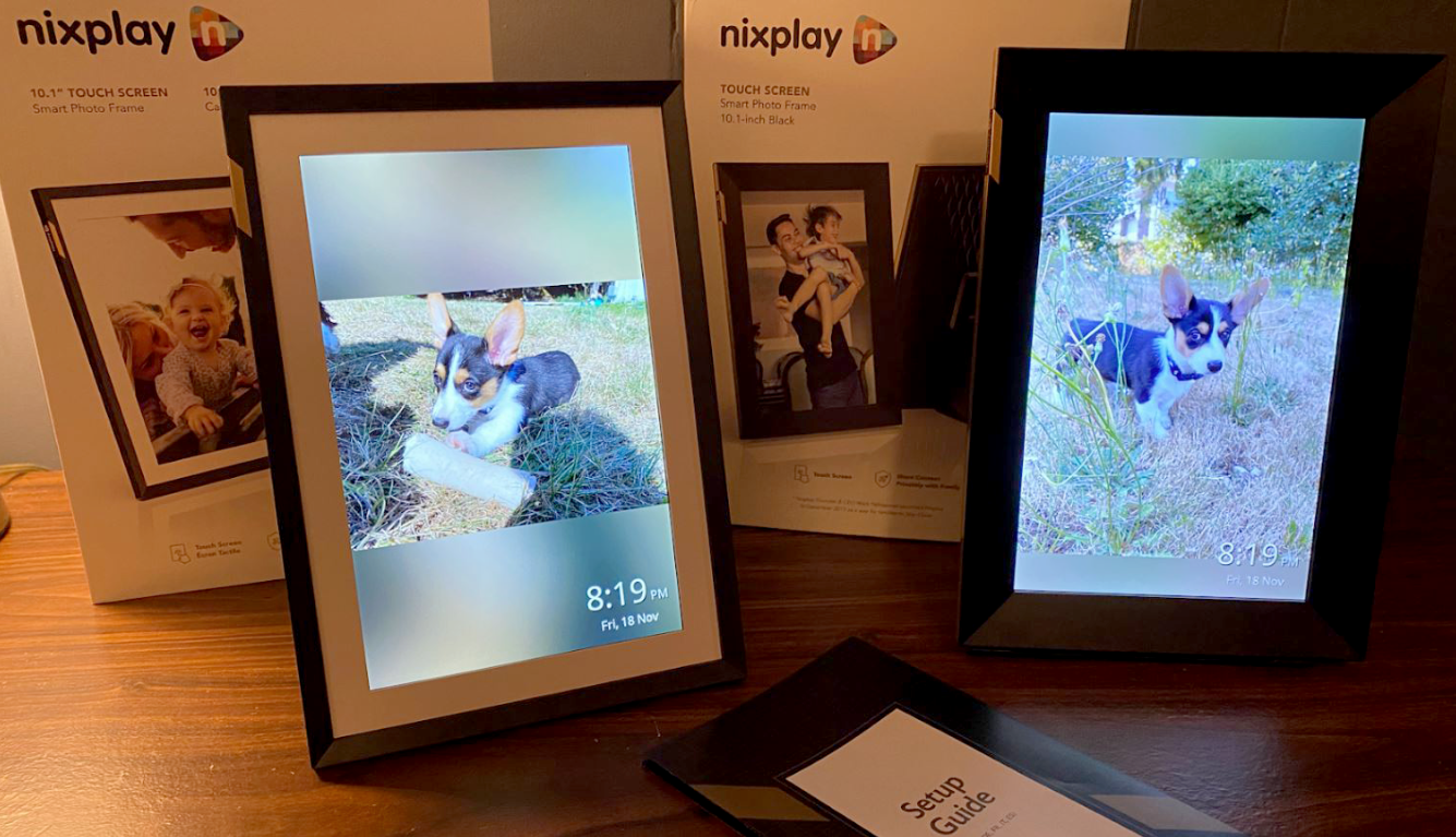 Nixplay Touch 10 New and Classic Side by Side in Portrait mode with the boxes behind them and the tatup manual in frame showing puppy photos