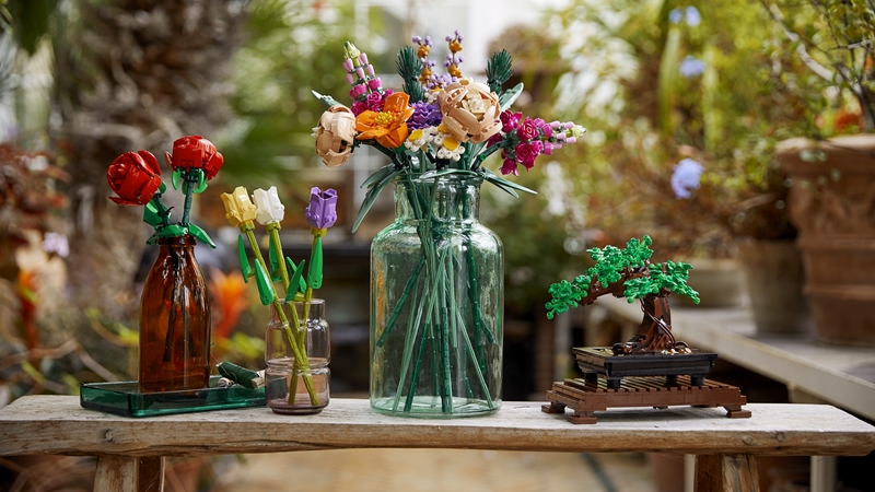 Four of the Lego Botanical collection sets lined up with flowers in glass vases and a garden backdrop blurred
