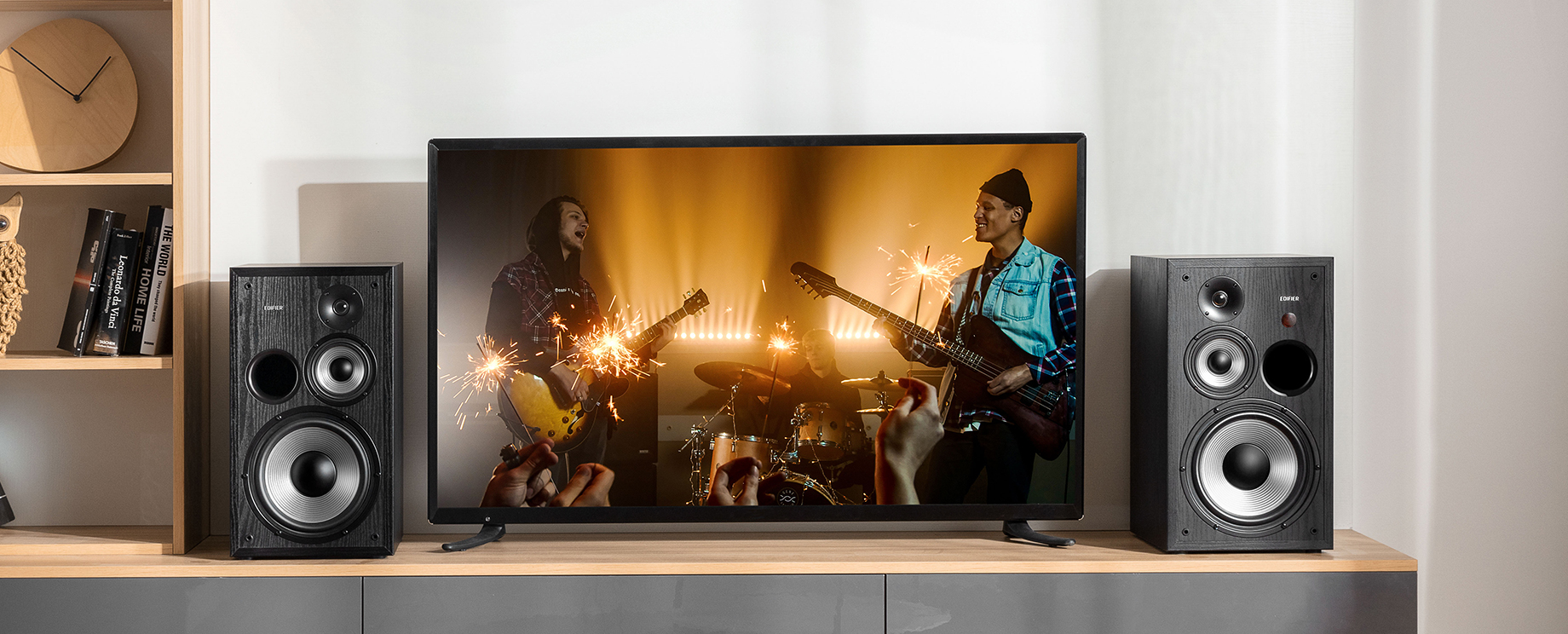 Two black Edifier home theatre speakers on either side of a smaller TV displaying a concert