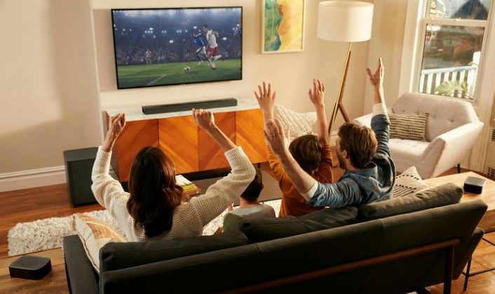 A set of a sound bar, surround sound speakers, and a subwoofer being used together for a family watching sports on their TV