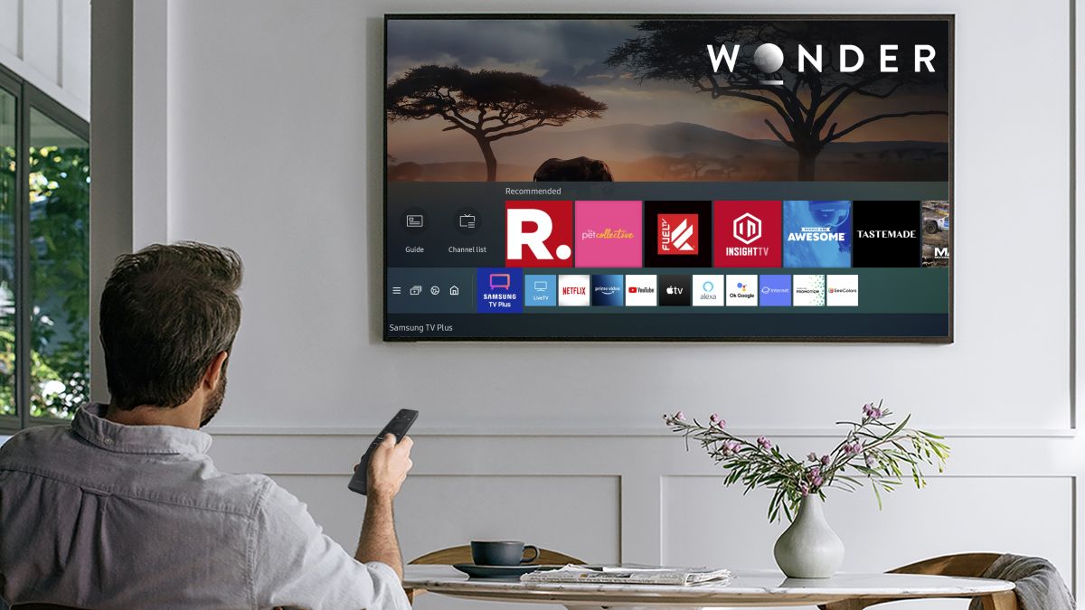 Smart TV being used with a remote by a man on a couch displaying potential channels to watch