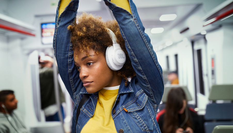 Woman using JBL headphones on a train with noise cancellation