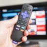 A photo of a hand holding a Roku remote control