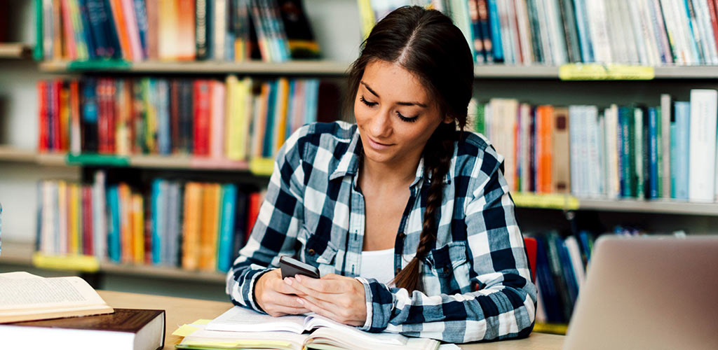 Étudiant dans une bibliothèque utilisant un téléphone.