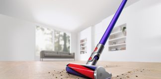 The Dyson V11 Absolute Pro Cordless Stick Vacuum is shown cleaning a hardwood floor in a white room. It makes a clean sweep through the dust and debris on the floor, leaving nothing behind it.