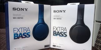 Two white boxes containing Sony WH-XB700 headphones. Each is labeled "SONY WH-XB700 EXTRA BASS." The boxes are outdoors in the sunlight. The left box contains a pair of headphones in blue while the box on the right contains a pair of headphones in black.