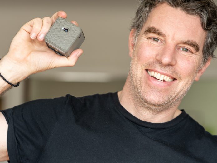 A photo of photographer Justin Morrison holding the XPRIT smart cube projector