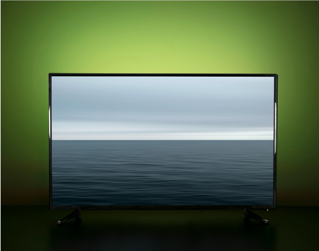 image of a TV with LED strip lights shining a green glow from the wall behind it