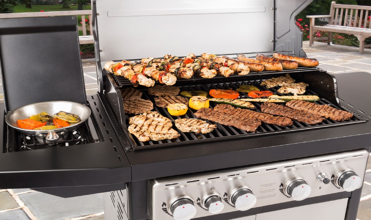 image of an open BBQ with the grill covered in cooking steaks, sausages, veggies, chicken, and skewers