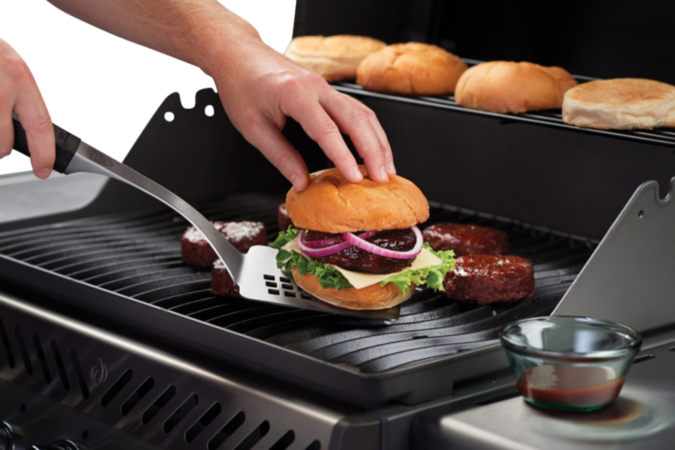 image of a person cooking burgers on a BBQ while burger buns are warmed on the warming rack