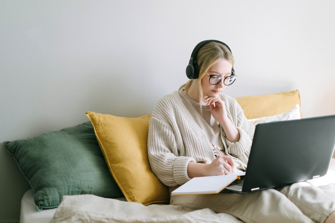 image of a woman working on a couch while wearing headphones
