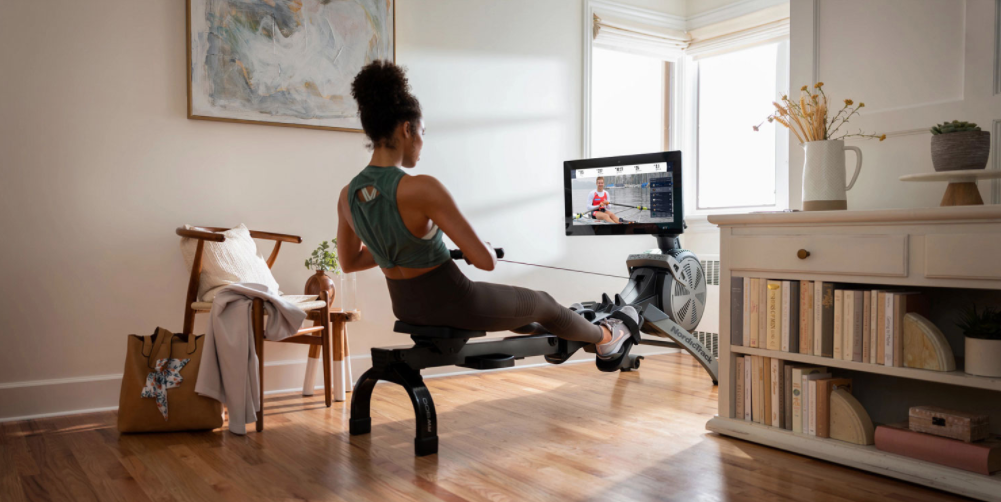 A woman watching a live class while rowing.