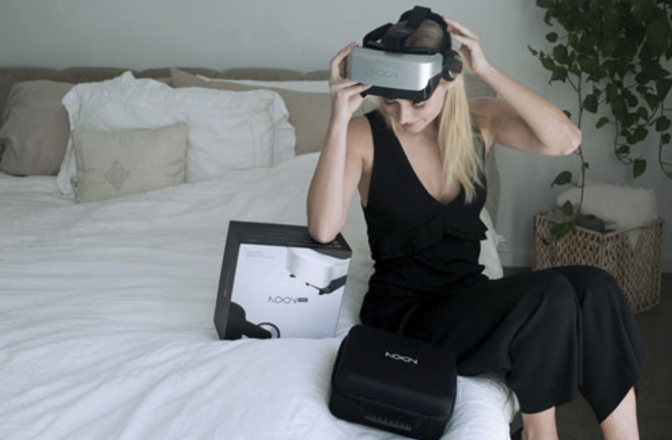 Woman sitting on bed wearing Noon VR headset.