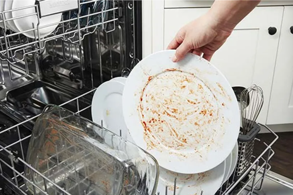 Hand putting a dirty dish in the dishwasher.