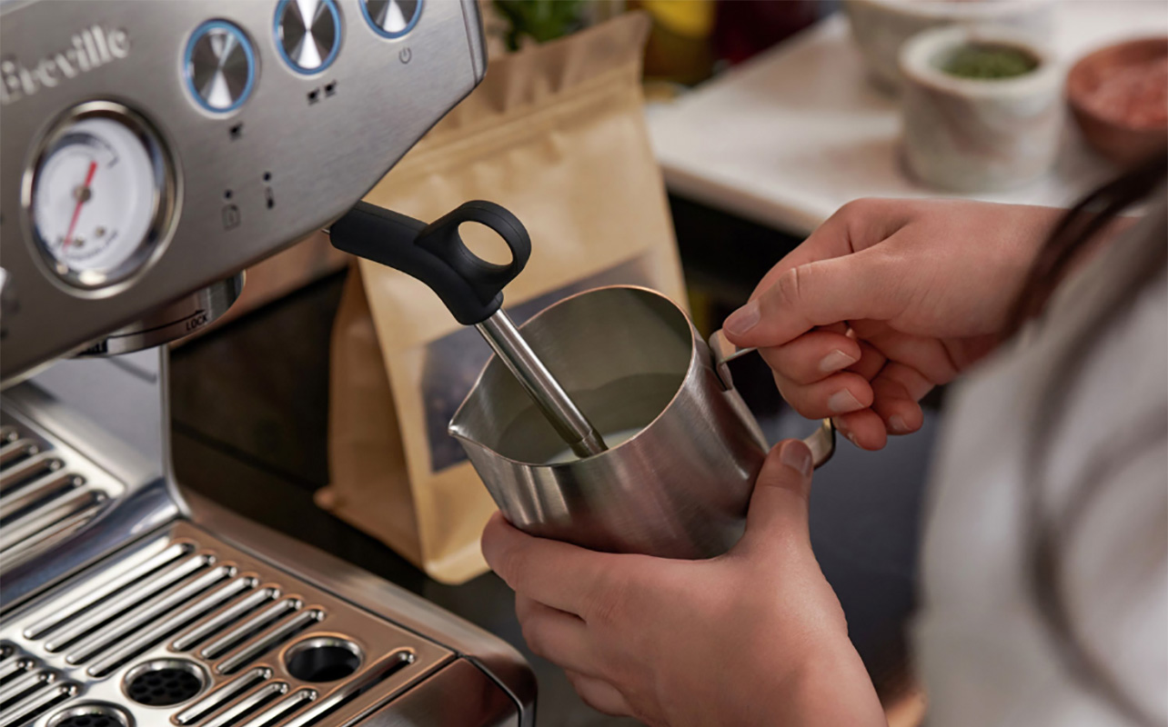 Hands using the milk frother in the Breville Barista Express Impress