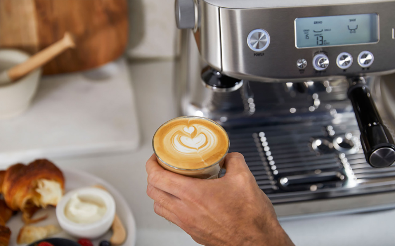 Gros plan sur une tasse de café avec l'art du latte, avec le Breville Barista Pro en arrière-plan.