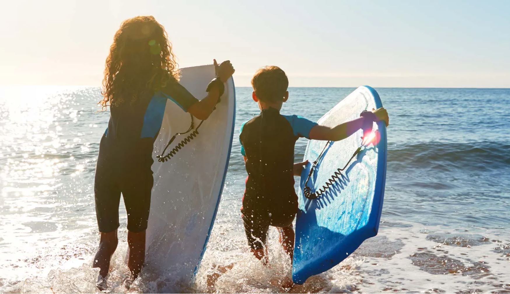 Two kids holding surboards by the water