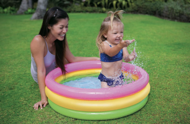 Mom sitting on the grass with a toddler in a mini kiddie pool.