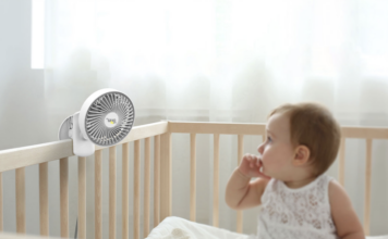 Baby in crib with a mini fan clipped to it.