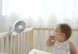 Baby in crib with a mini fan clipped to it.