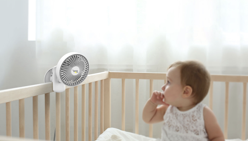 Baby in crib with a mini fan clipped to it.