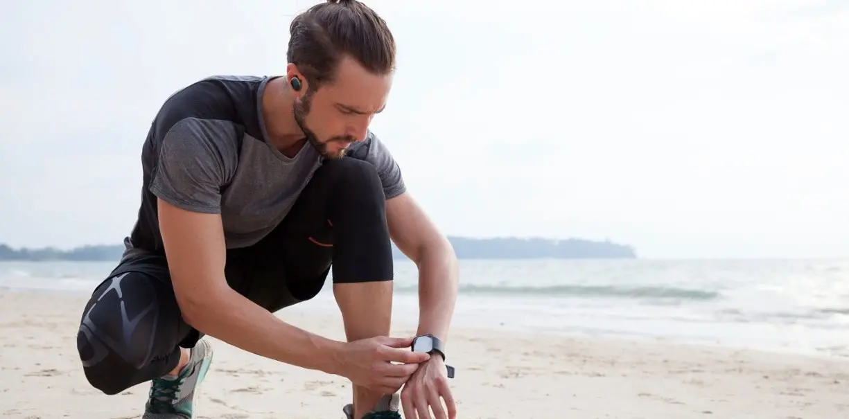 Man wearing JBL waterproof headphones while at the beach going for a jog
