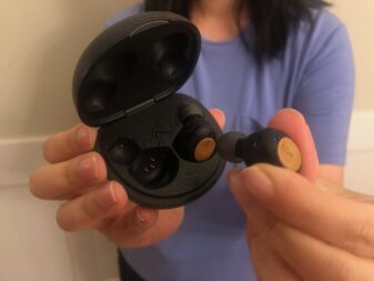 Woman holding one Marley Champion 2 earbud with the other earbud in the opened charging case. 