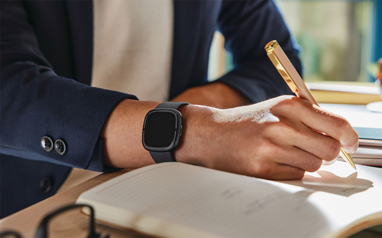 A hand writing with a Fitbit Sense 2 on the wrist.