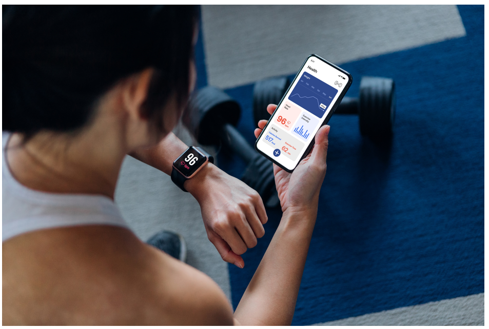 Woman looking at smartwatch and smartphone fitness metrics.