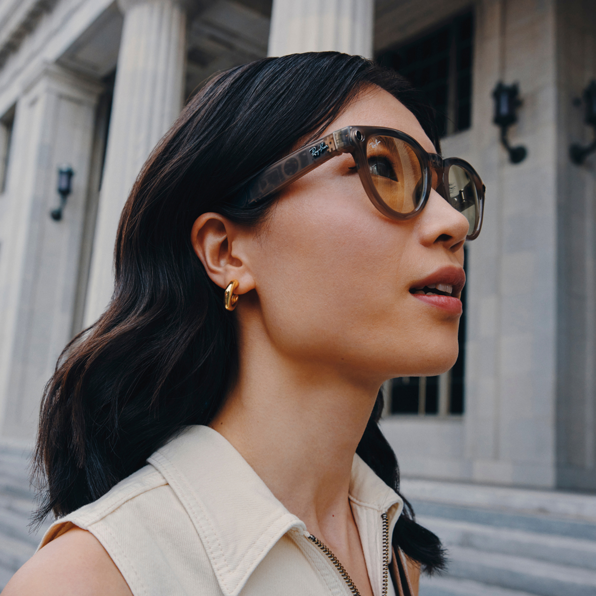 Woman wearing Ray-Ban Meta Smart Glasses in front of building.