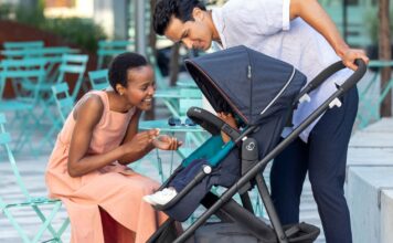 A woman crouching to look at a baby in a stroller a man is pushing.