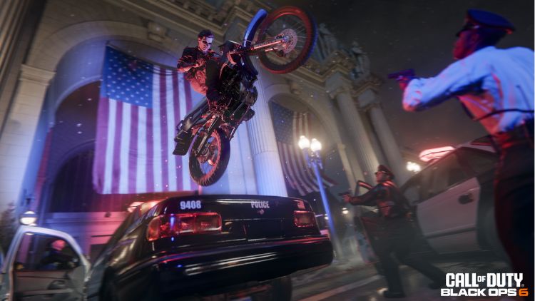 A man on a motorcycle jumps over police cars with the American flag in the background.