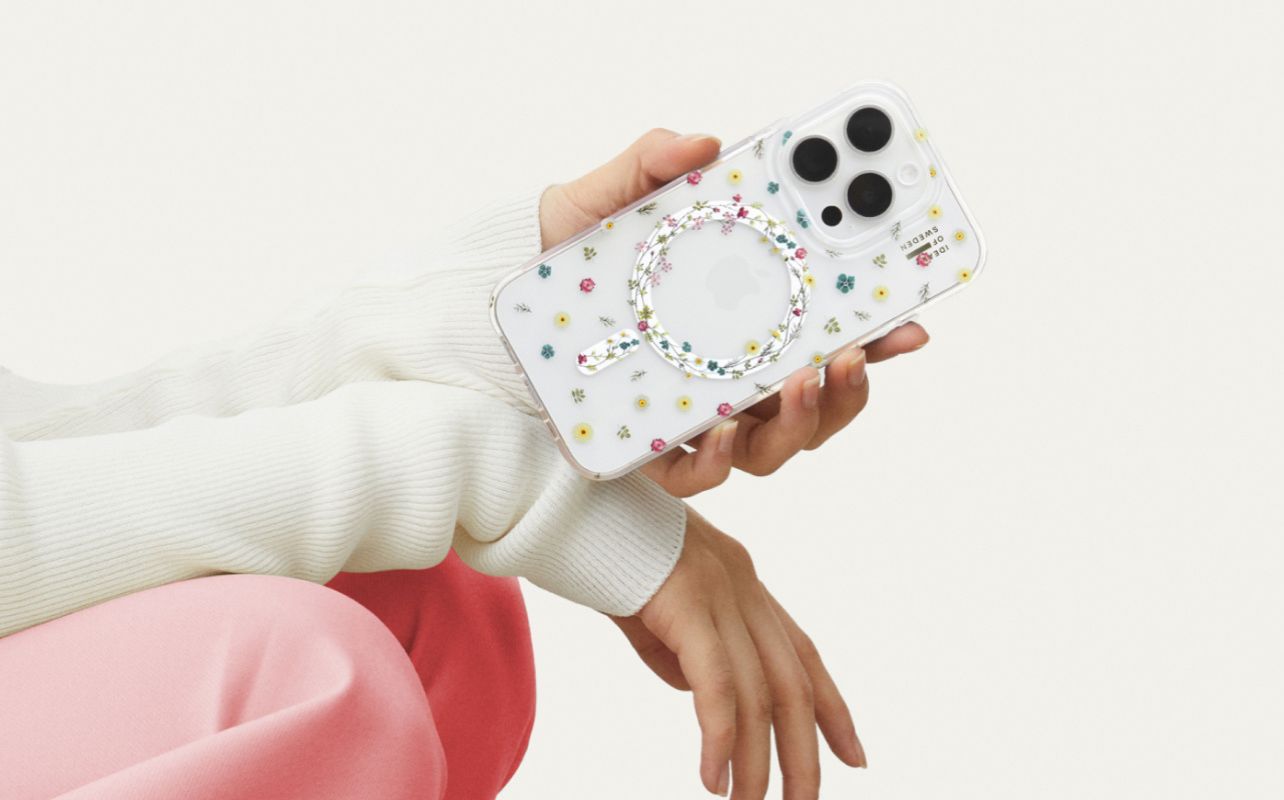 A hand holding an iPhone 16 with the Petite Floral clear Ideal of Sweden phone case against a white background.