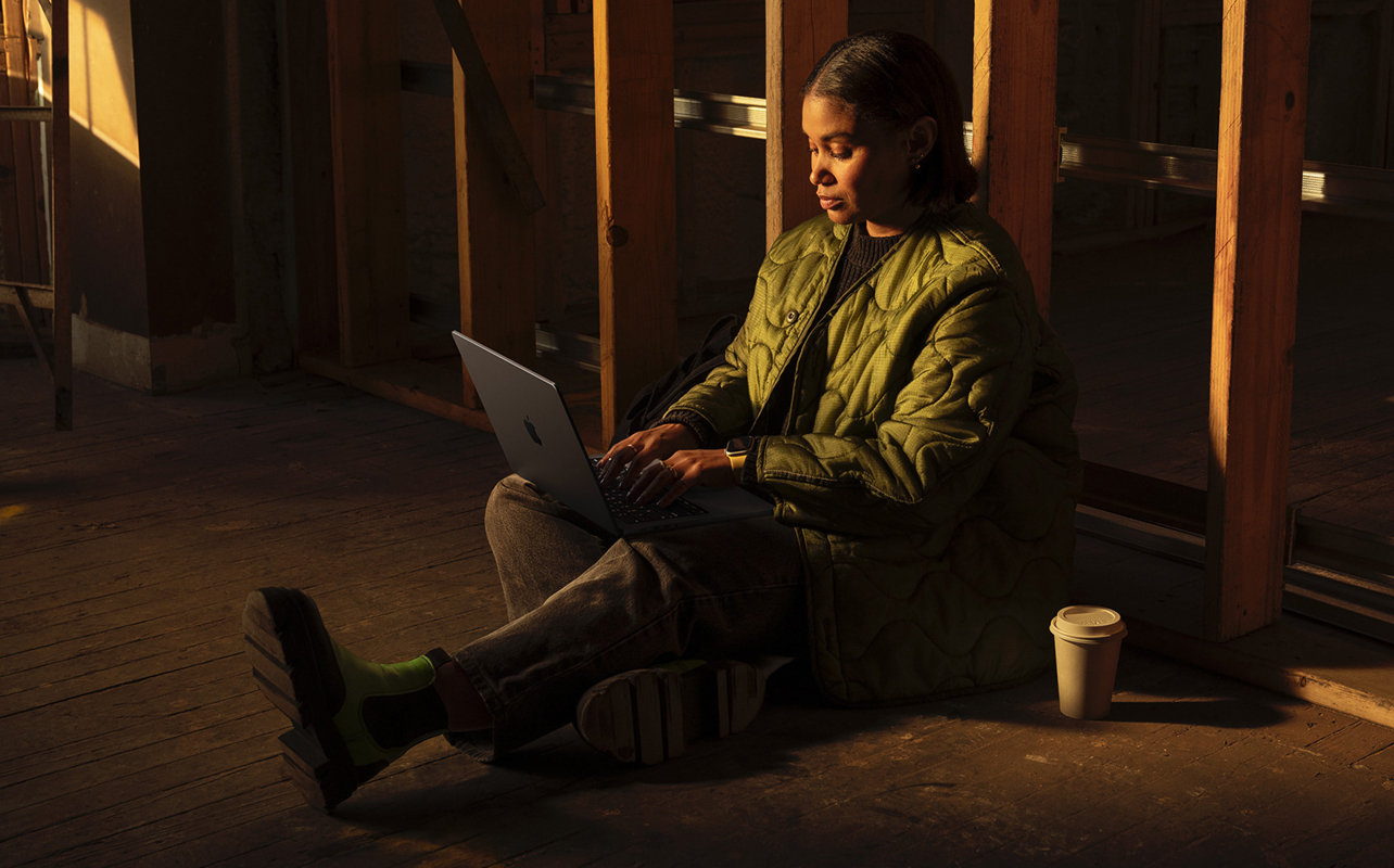 Woman sitting on ground working on a laptop.