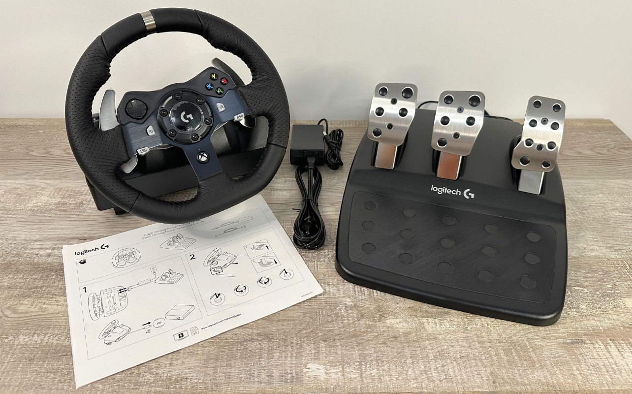 The Logitech G920 racing wheel, pedals, paper cable and instructions on a well lit desk.