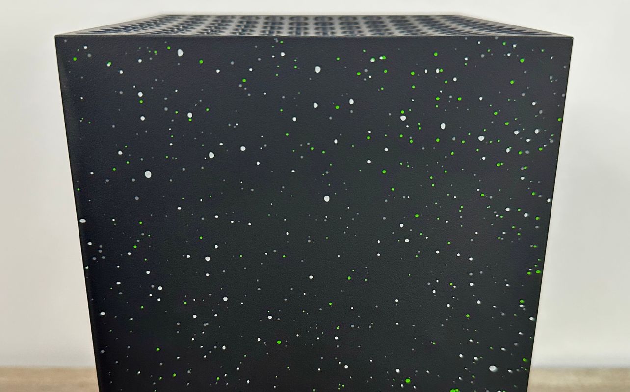 A close up of the Xbox Series X Galaxy Black Special Edition's speckled pattern sitting on a gray wood desk.