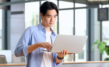 Man holding laptop in hand while using trackpad.