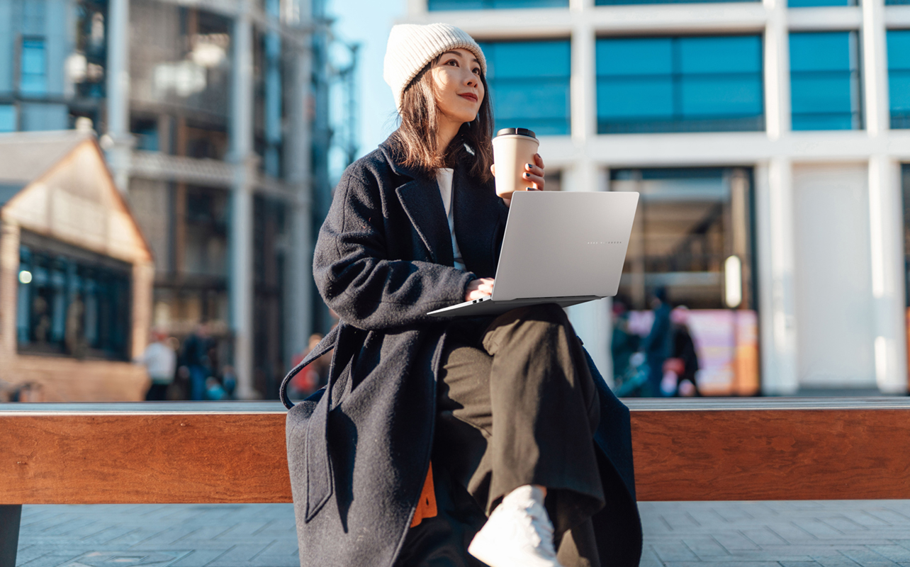 Young woman resting laptop on lap outside.