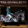 TCL 115QM7K TV on a stand at a CES 2025 showcase.