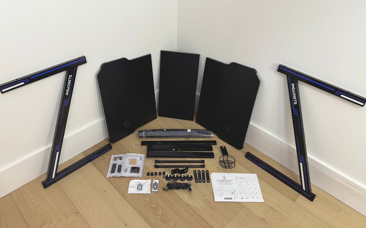 The IMGadgets Z-Shaped Gaming Desk is unboxed with components on a wood floor.